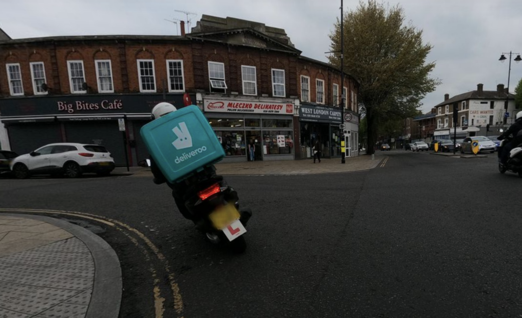 A motorcyclist takes the corner opposite the clocktower at speed, illustrating how the junction (without a signalled pedestrian crossing) prioritises moving motor vehicles at speed